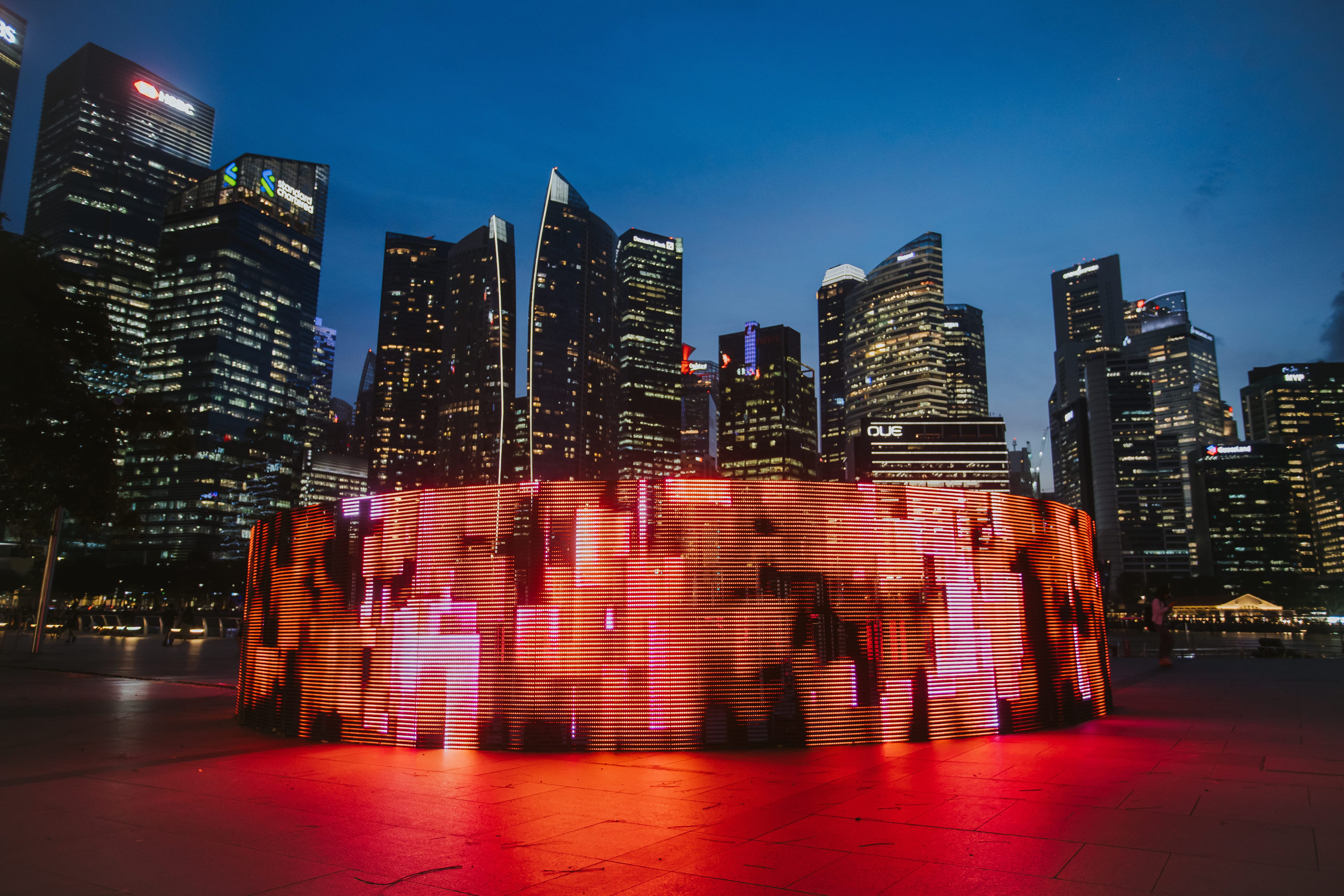A glowing blue light encircling a cylindrical outdoor installation at dusk.